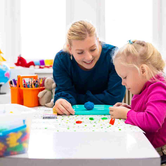 OT helping a young girl with fine motor skills by playing a game.