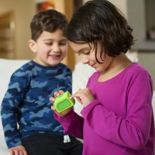 A child's hand gently holding the Lil Nipper Child clipper, demonstrating its ergonomic design. He brother behind her smiling. They are both laughing and smiling.