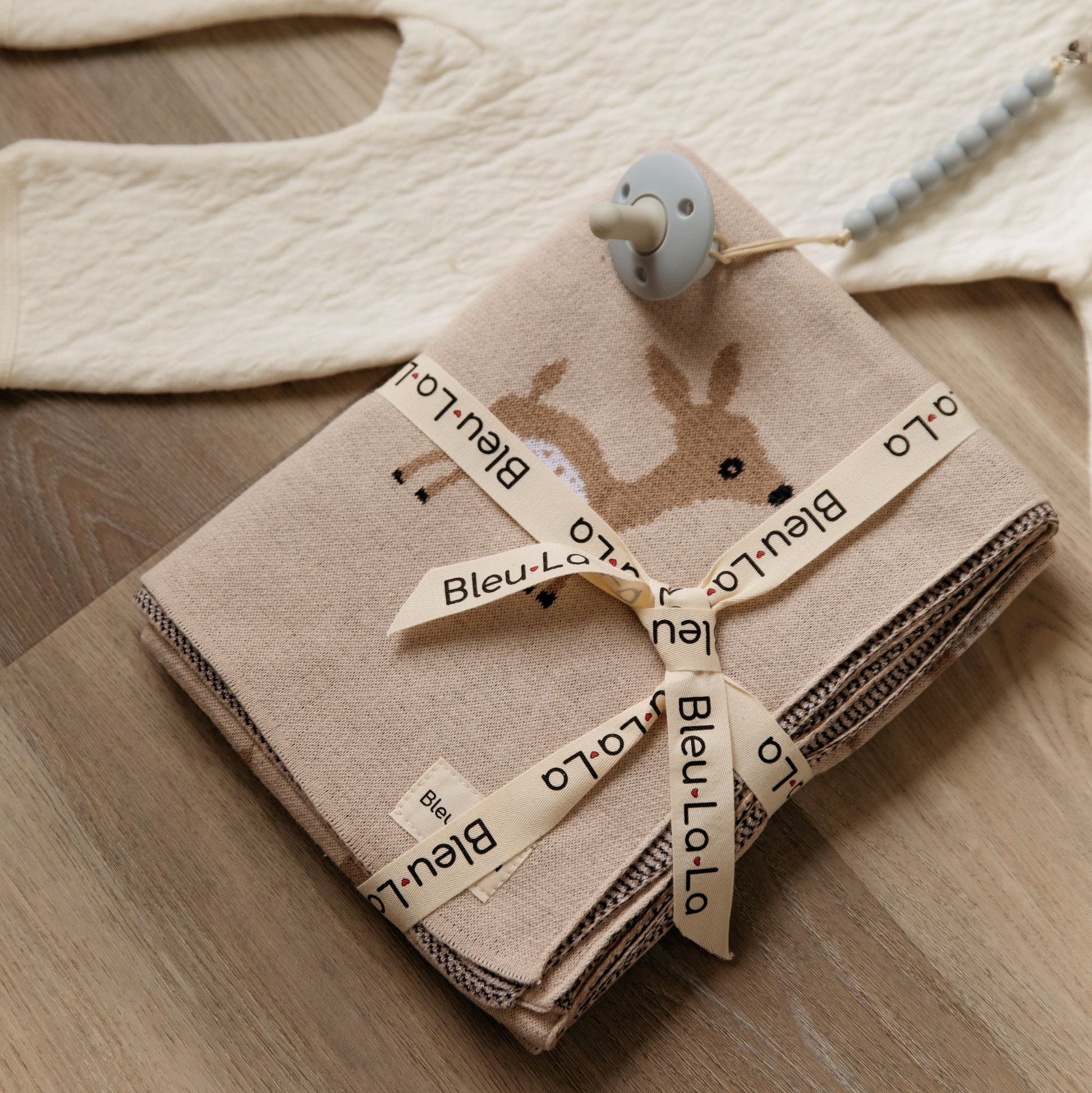 Folded baby blanket with deer design and 'Bleu-Lo' branding on a wooden surface