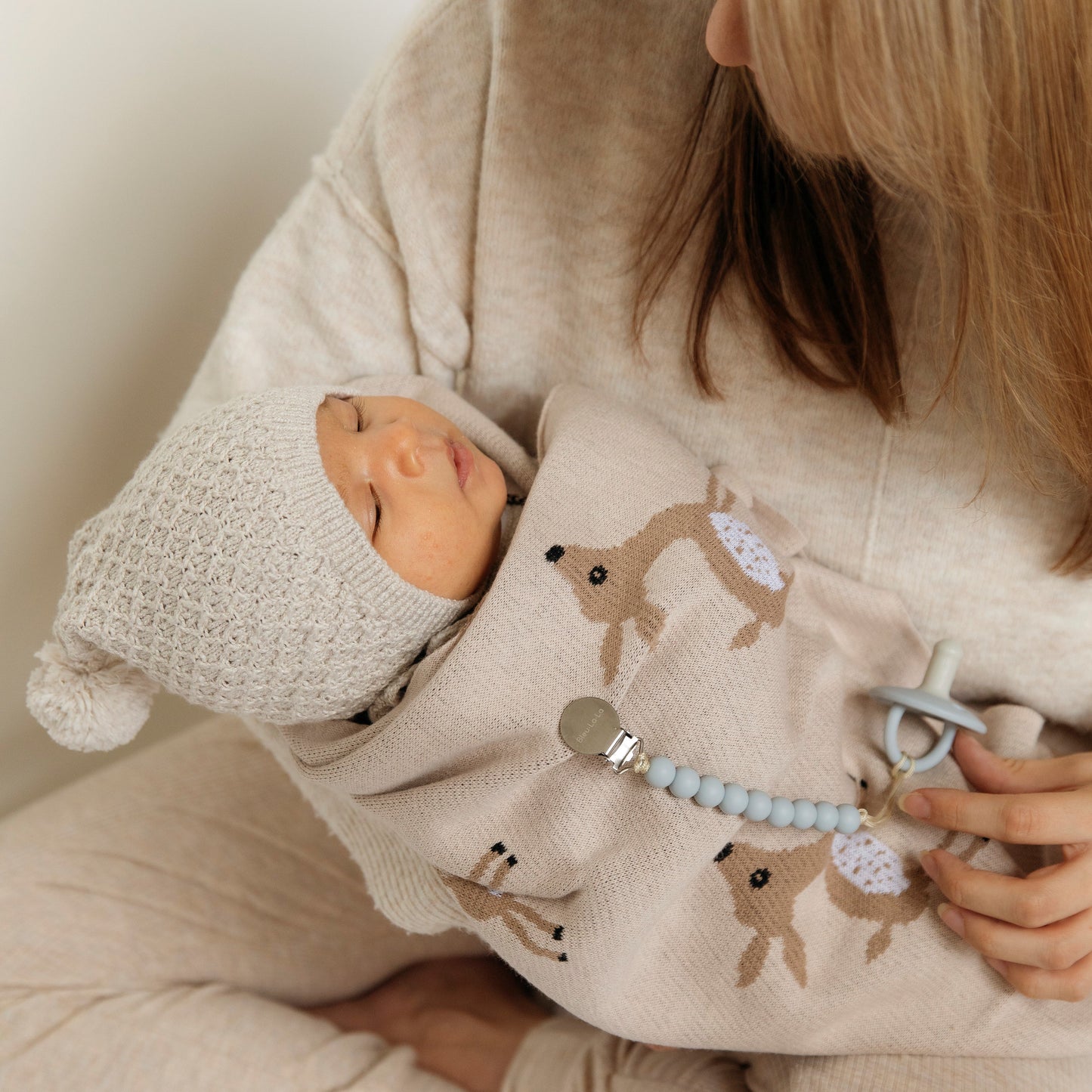Person holding a baby doll and a cushion with deer patterns, wearing a beige outfit.