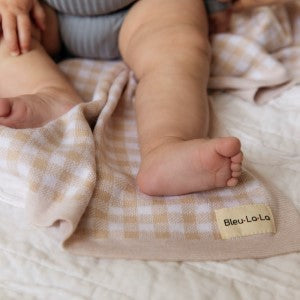 Close-up of baby feet on a checkered blanket with 'Bleu Lolo' label