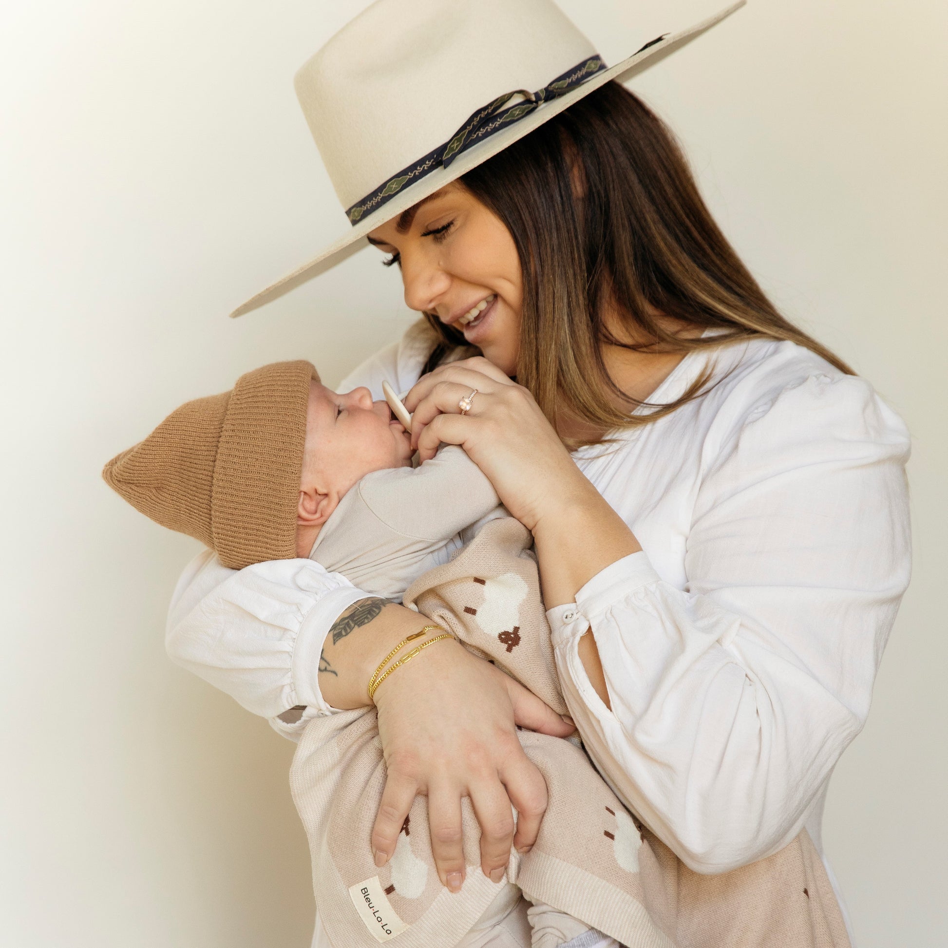 A woman wearing a beige hat holding a baby against a plain background