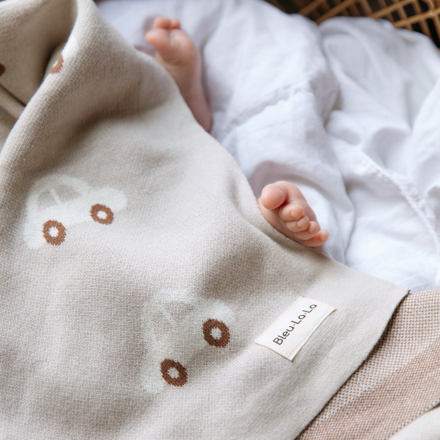 Baby feet peeking out from under a beige blanket with brown floral patterns, featuring the brand 'Bleu-La-La'