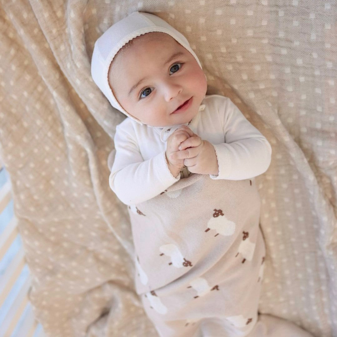 Baby in a white outfit with a hood lying on a textured blanket