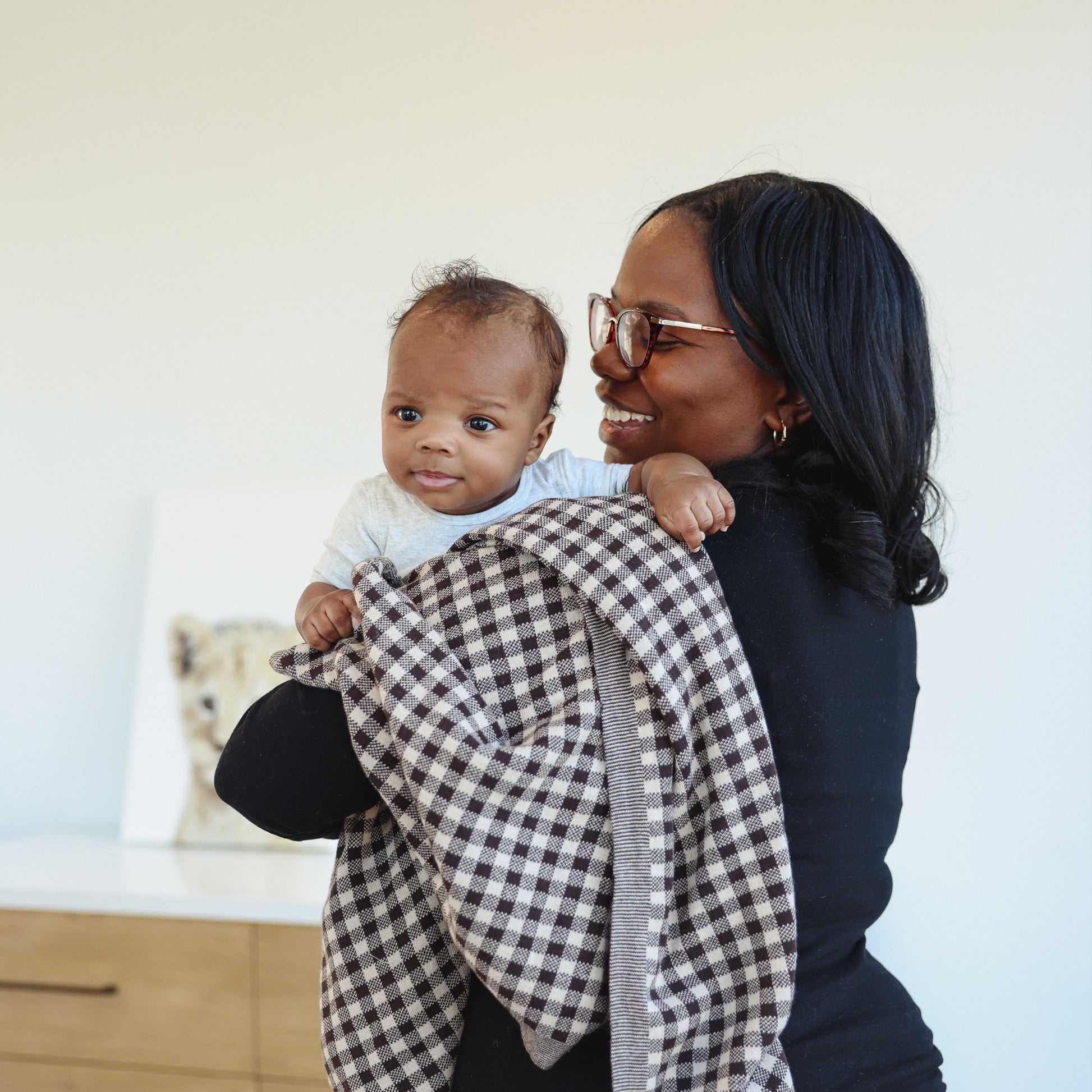 Woman holding a baby wrapped in a checkered blanket indoors