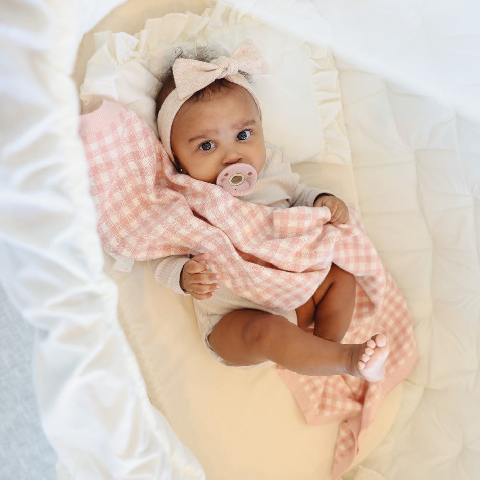 Baby wrapped in a pink checkered blanket with a pacifier, wearing a headband.