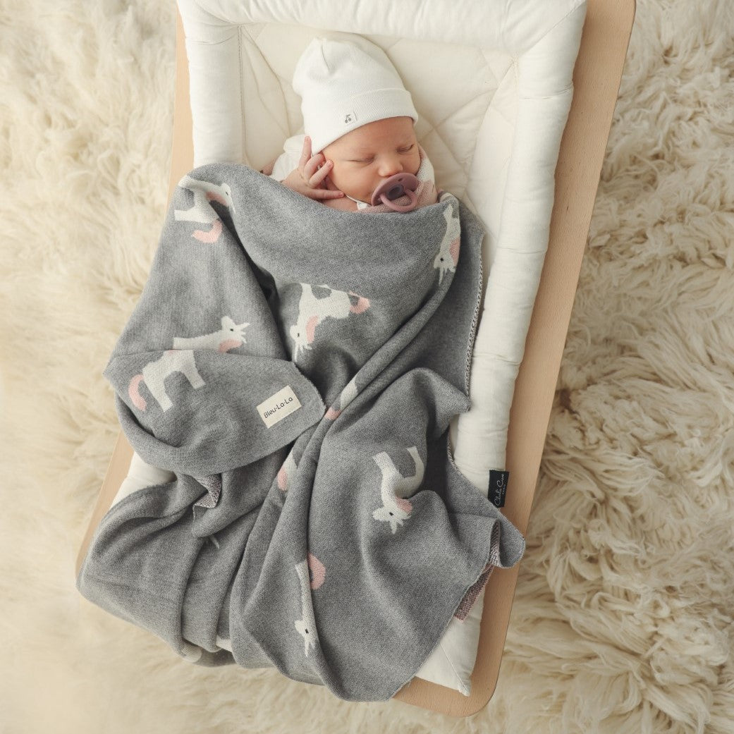 Newborn baby wrapped in a gray blanket with animal patterns on a fluffy white surface.