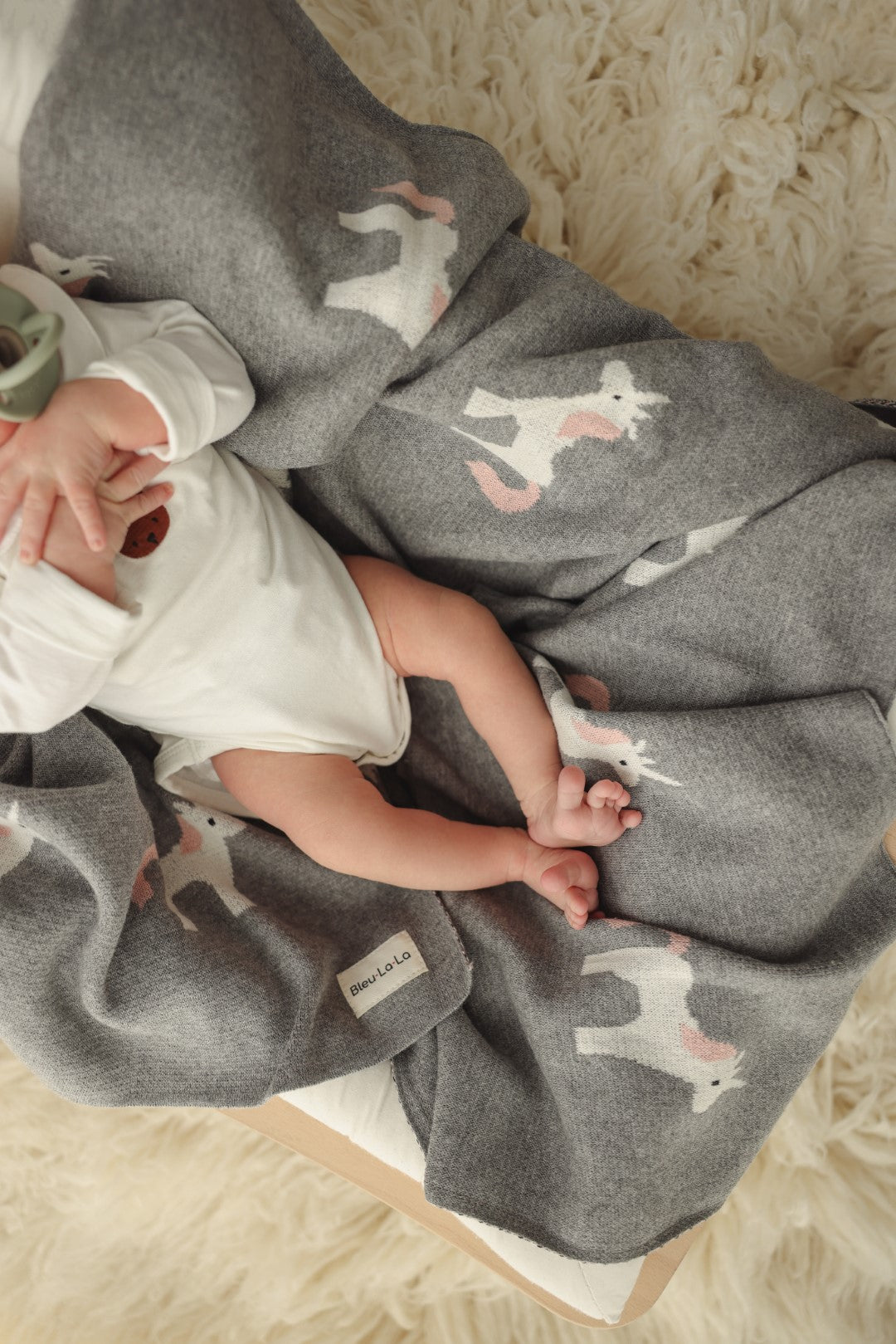 Baby wrapped in a gray blanket with unicorn patterns on a soft surface