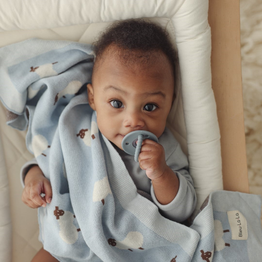 Baby lying on a bed with a blue blanket from 'Bleu La La'