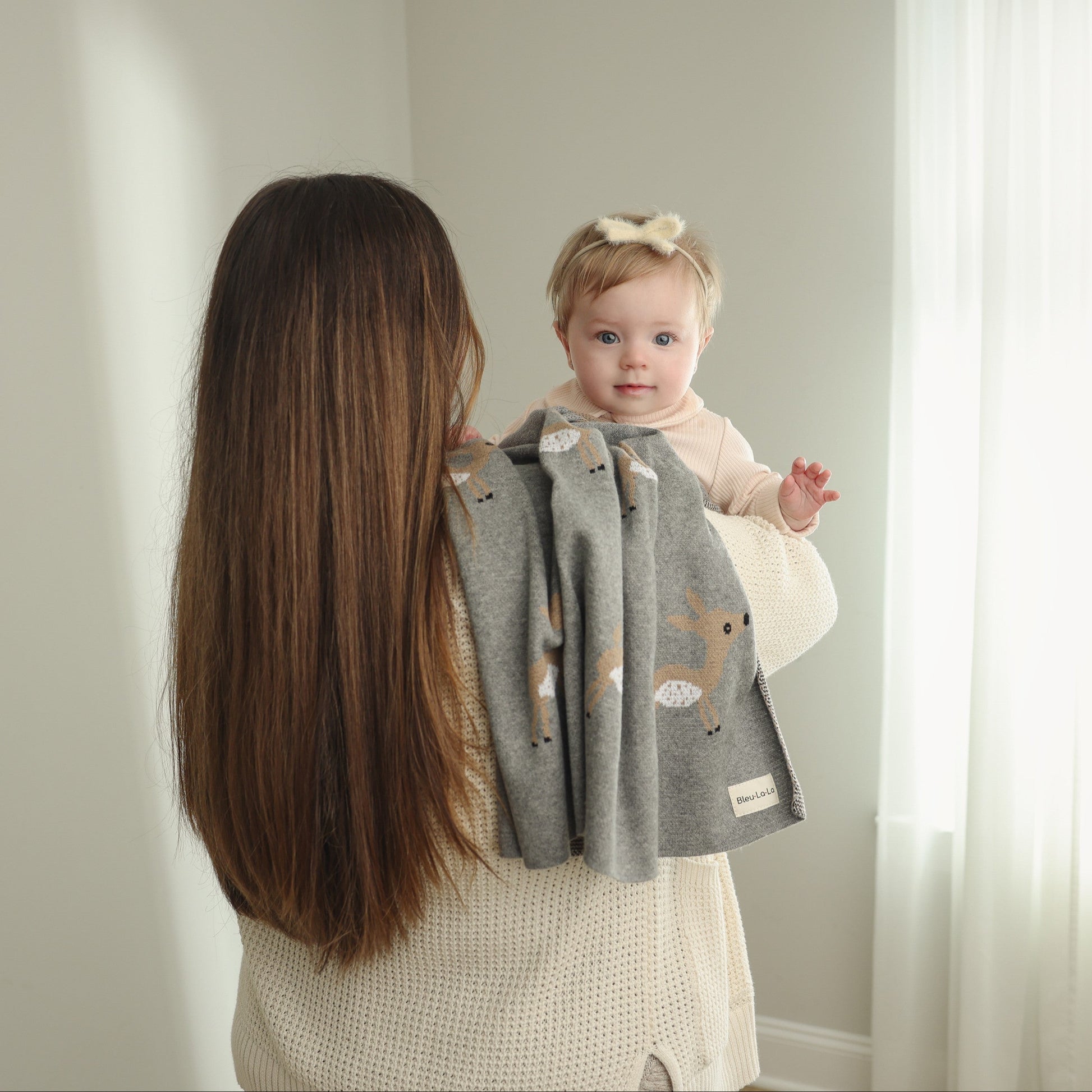 Woman holding a baby wrapped in a gray blanket with animal patterns against a neutral background
