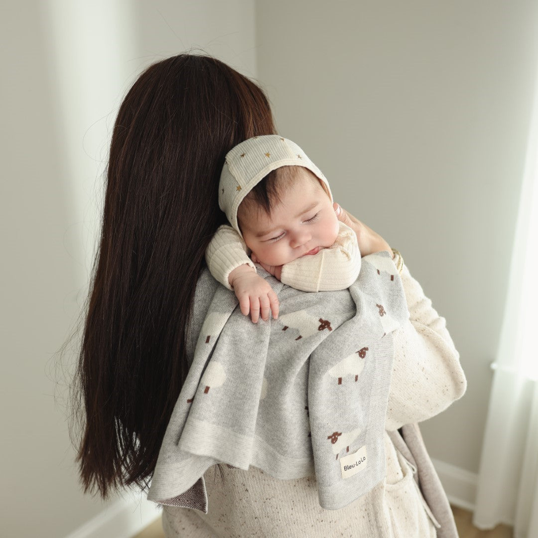 Woman holding a baby wrapped in a gray blanket with a neutral background