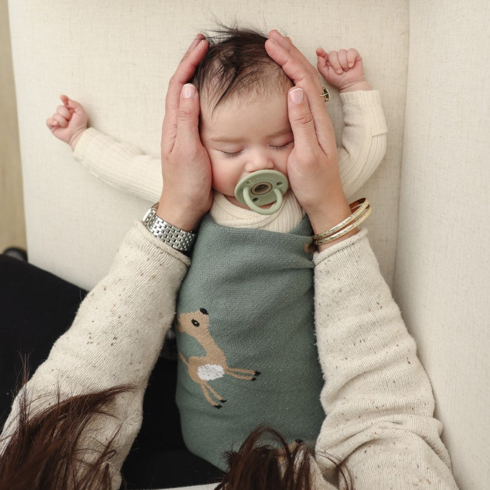 Baby wearing a bib with a deer design, held by a person in a cozy setting.