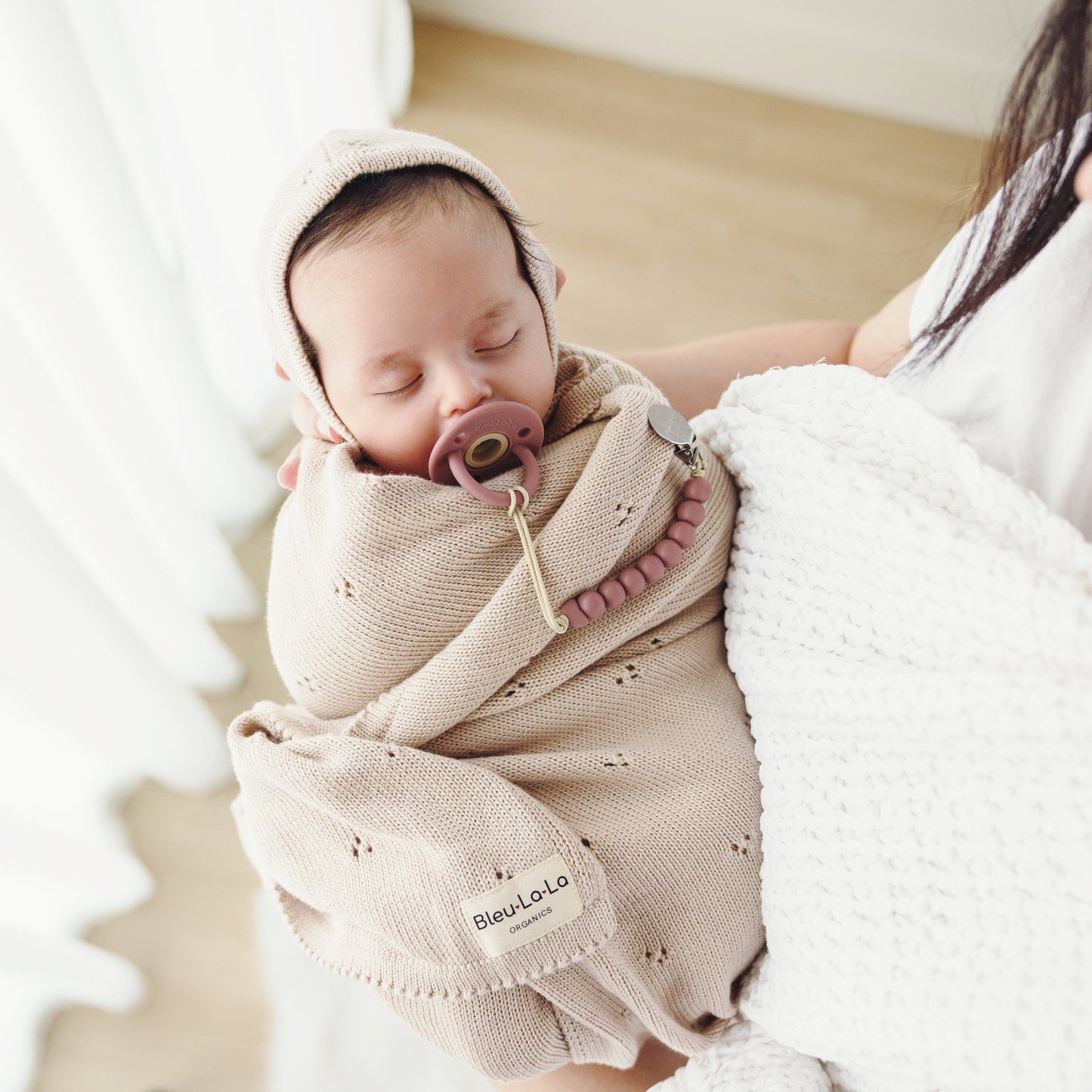 Newborn baby wrapped in a beige swaddle with a pacifier, held by a person.
