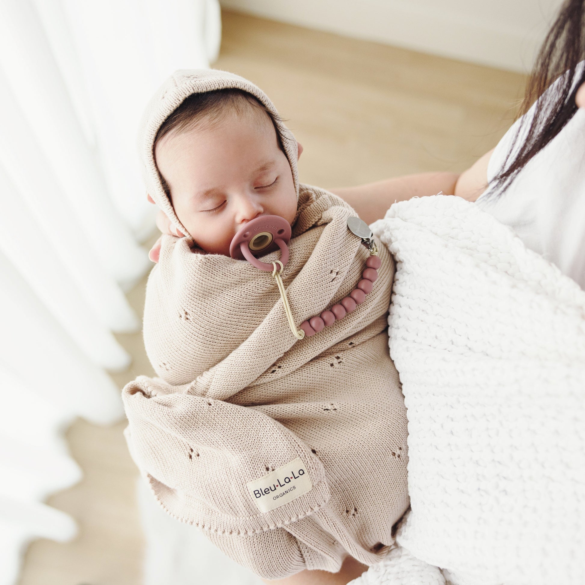 Newborn baby wrapped in a beige swaddle with a pacifier, held by a person.