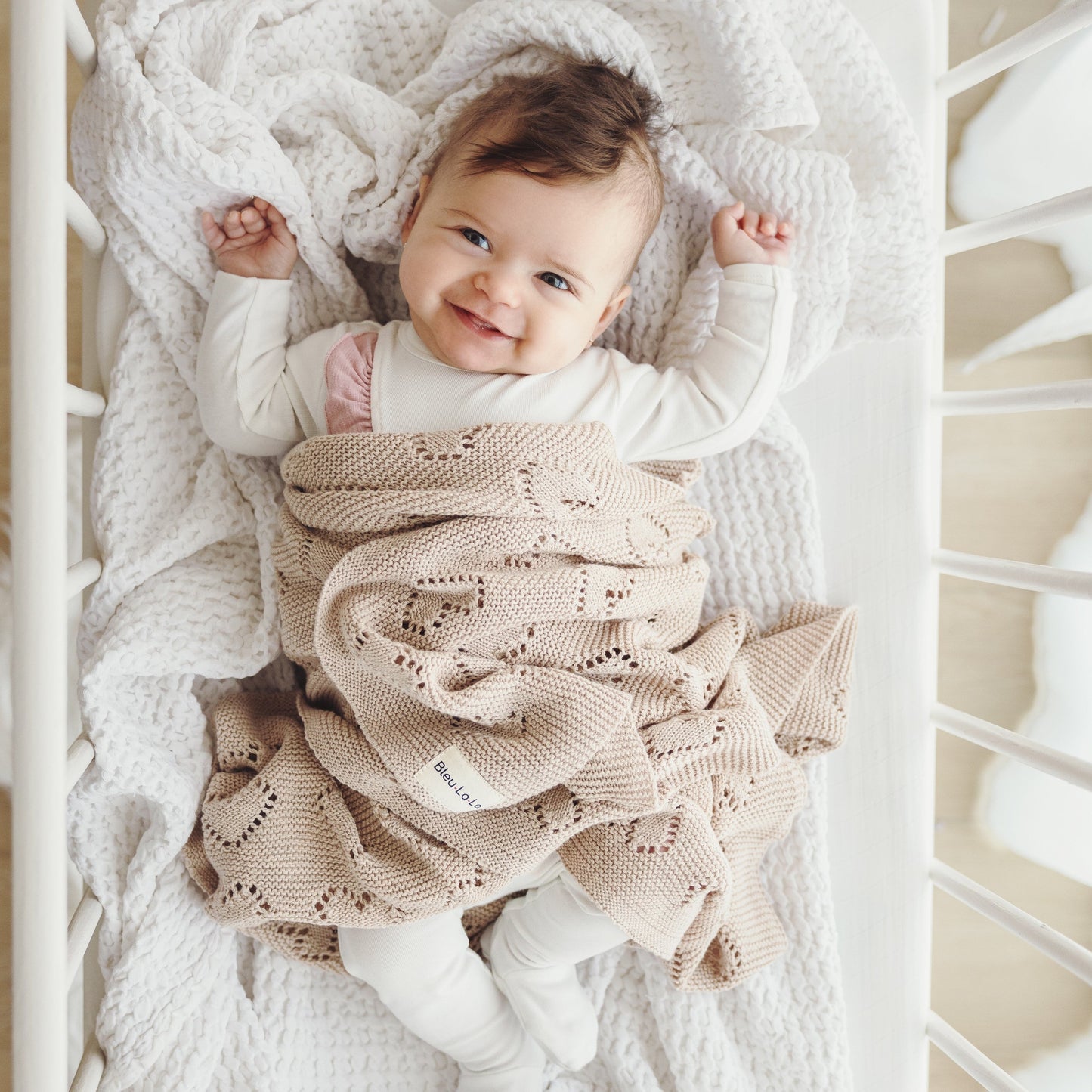 Baby wrapped in a beige knitted Bleu-la-la blanket in a crib