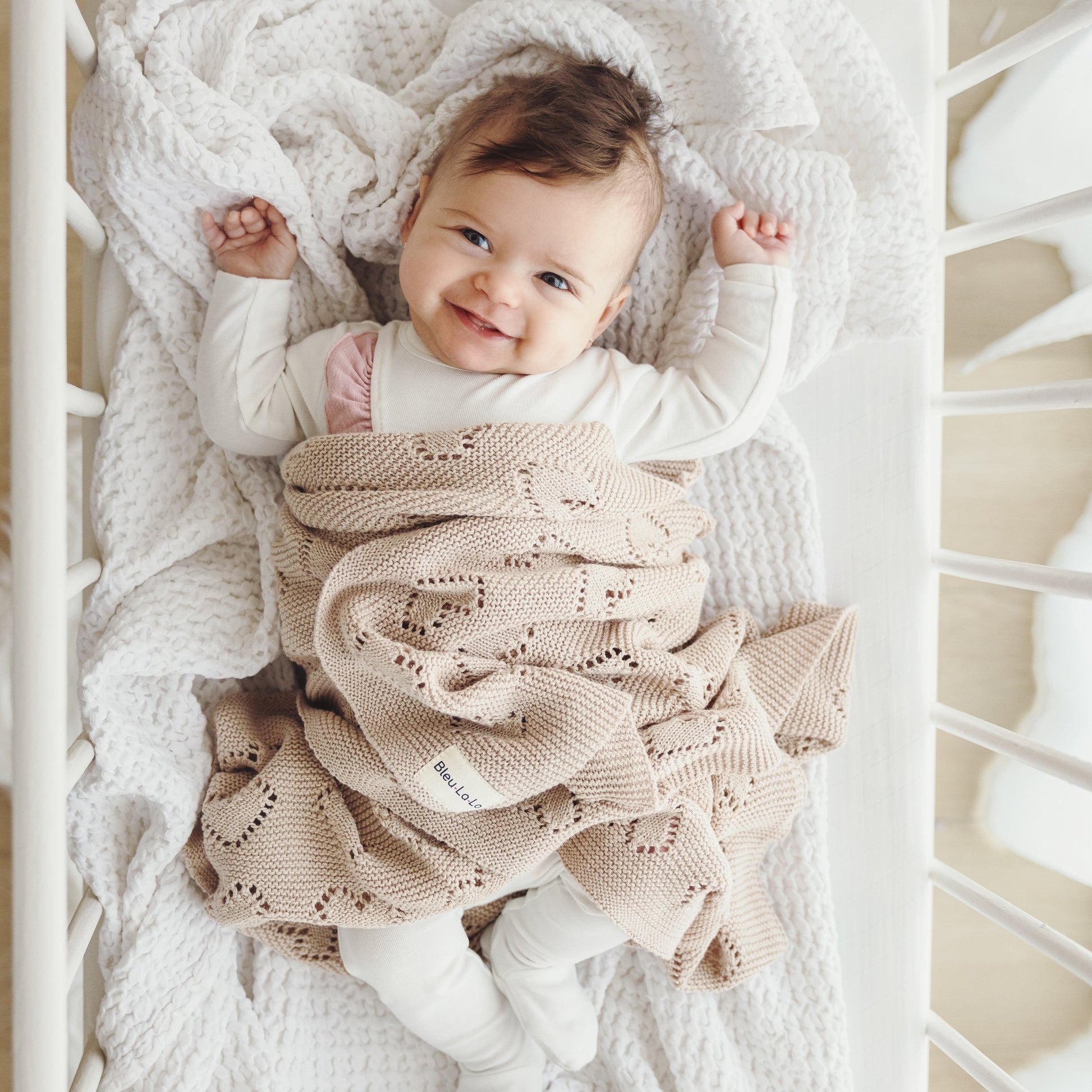 Baby wrapped in a beige knitted Bleu-la-la blanket in a crib
