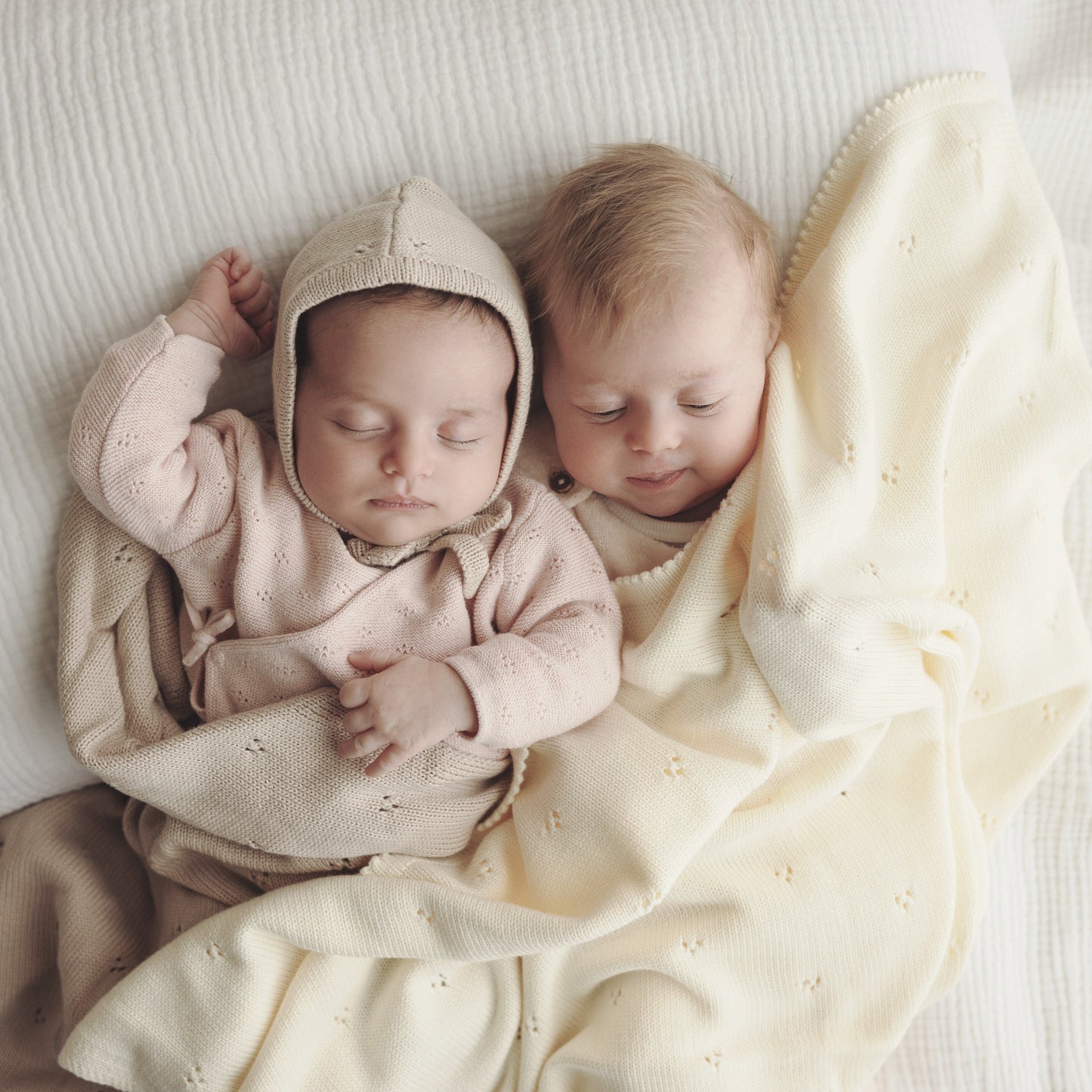 Two babies wrapped in a blanket on a soft surface