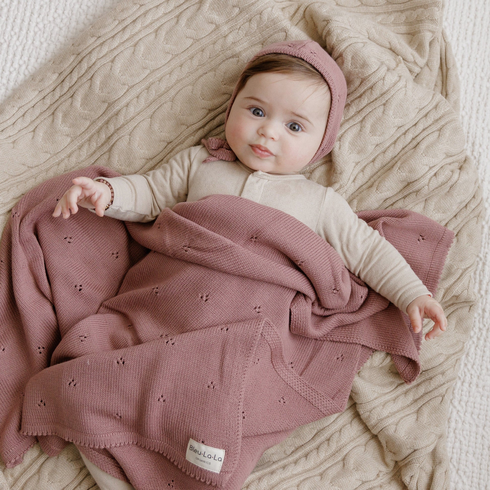 Baby wrapped in a pink blanket with a matching headband, lying on a textured surface.