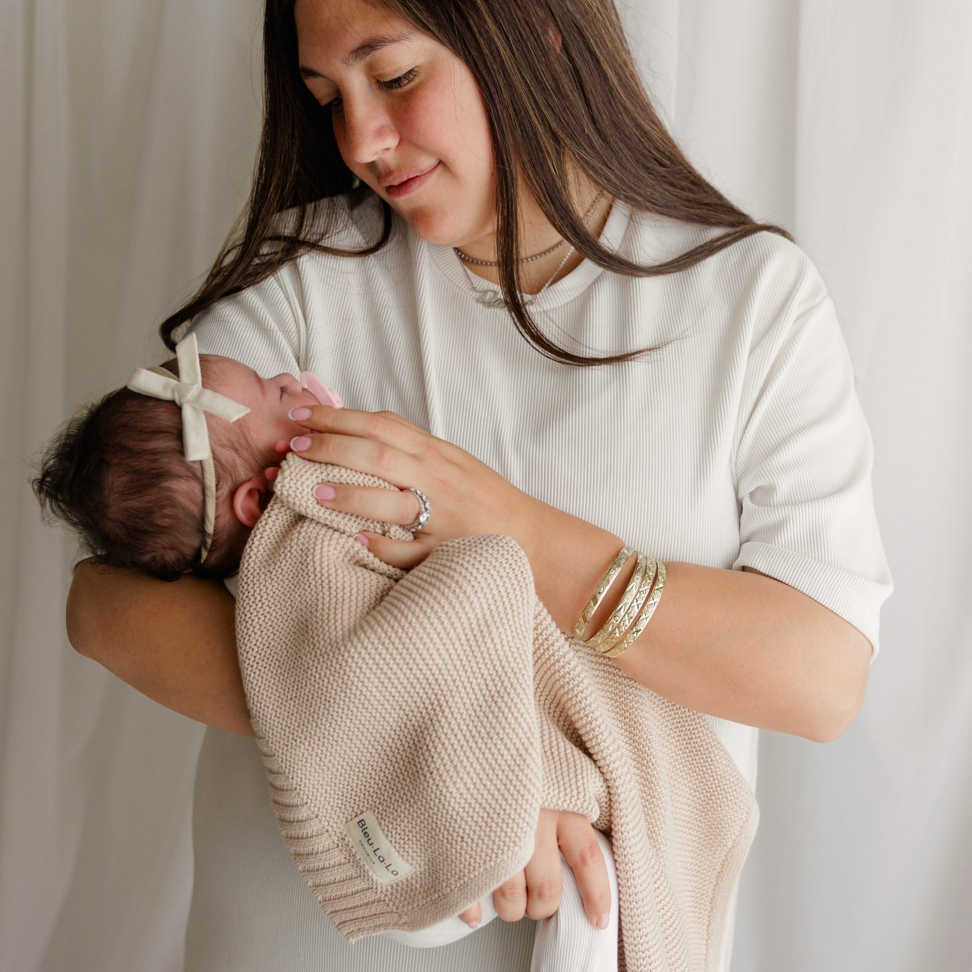 Woman holding a baby wrapped in a beige Blue-La-La blanket against a plain background
