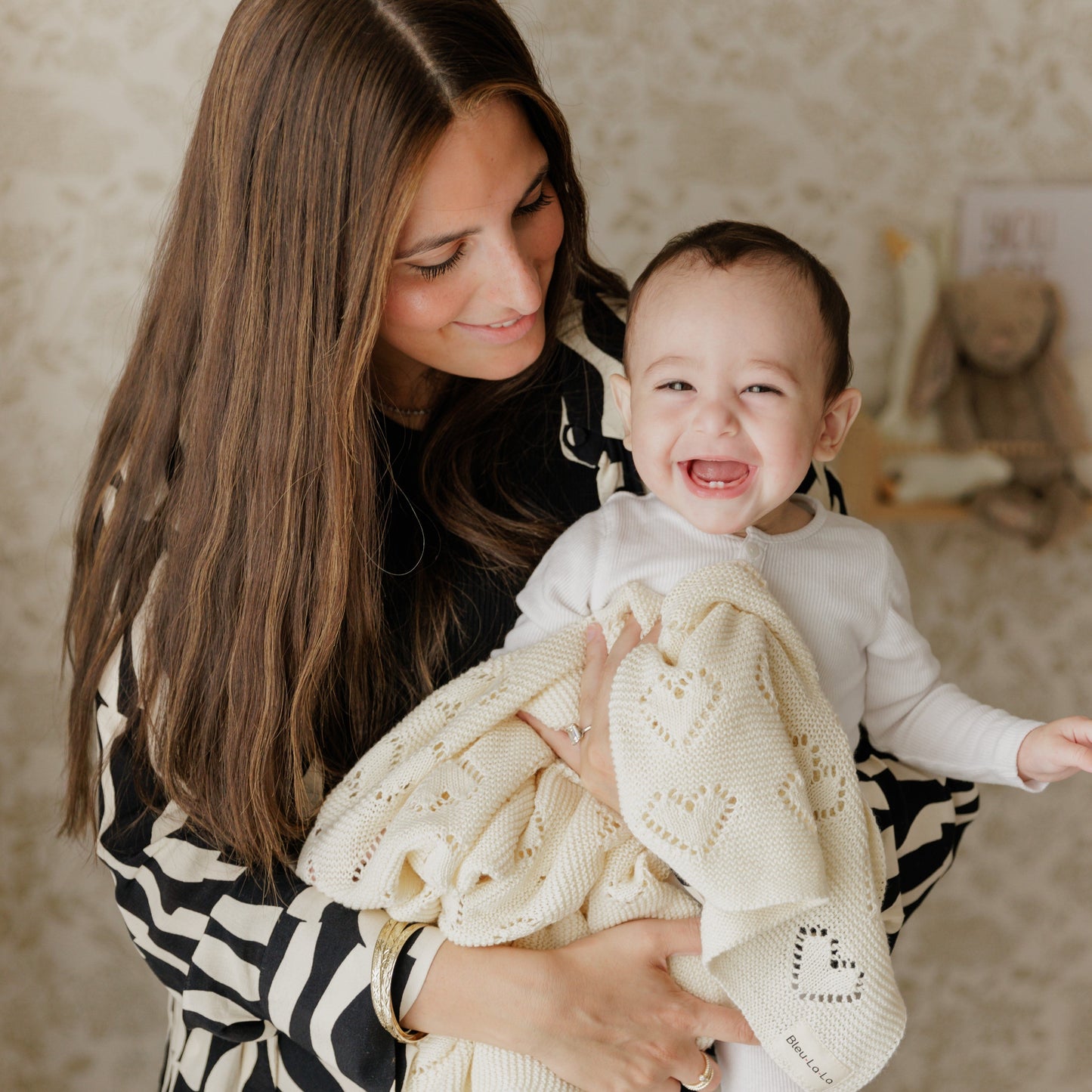 Woman holding a baby wrapped in a white Bleu-la-la  blanket with a heart pattern, smiling.