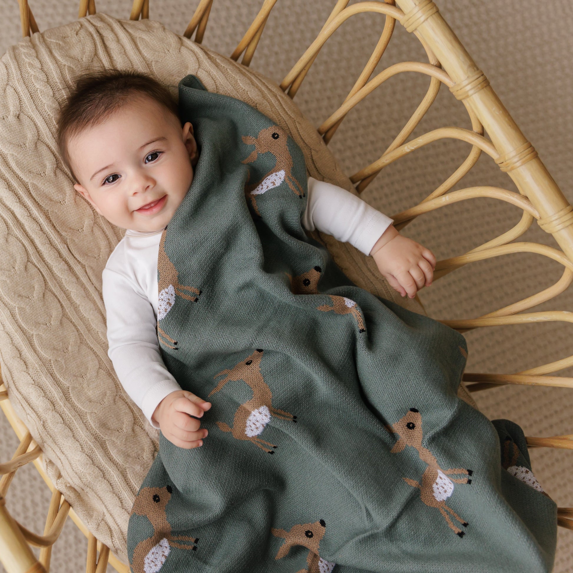 Child wrapped in a green blanket with deer patterns, sitting in a wicker chair.