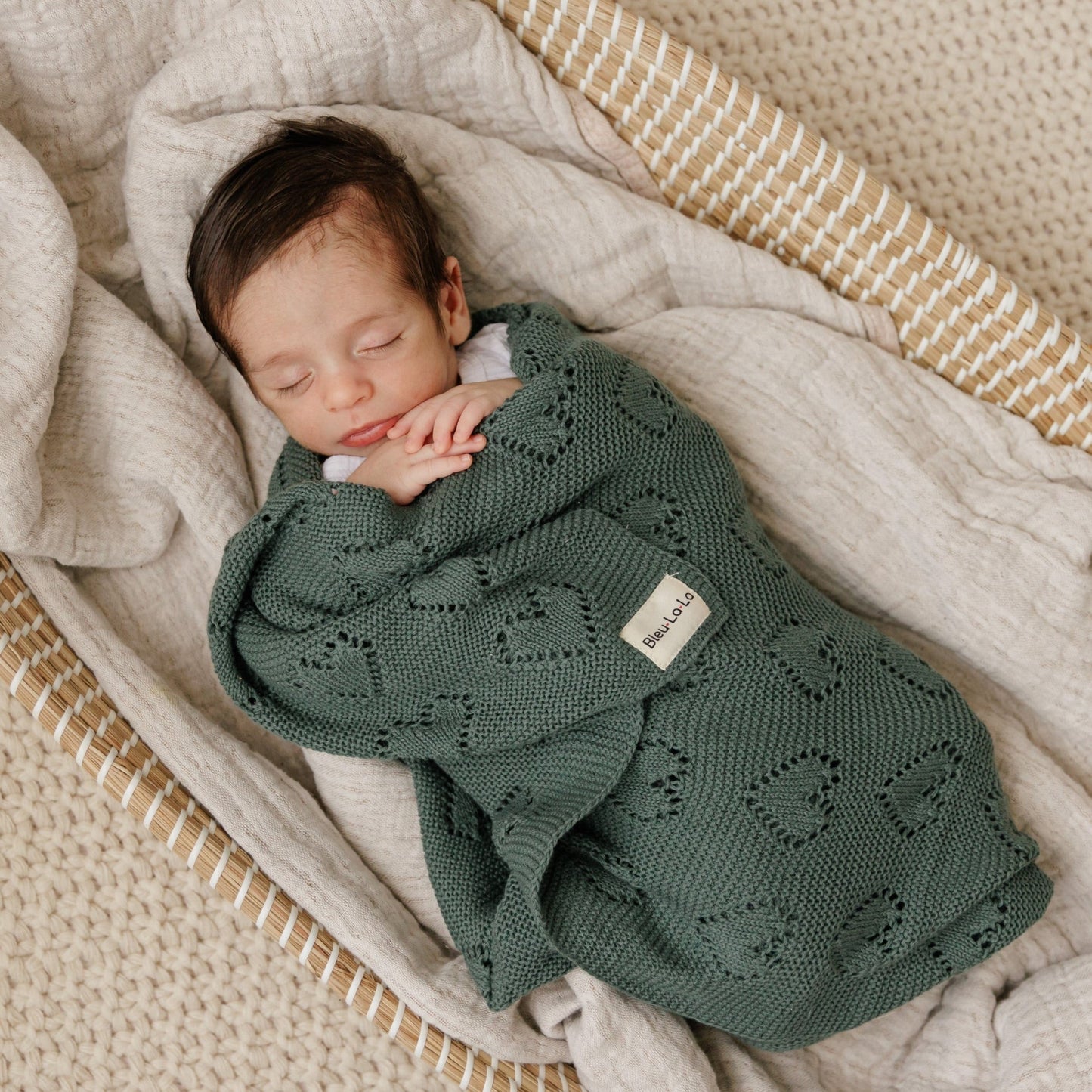 Newborn baby wrapped in a green knitted Bleu-la-la  blanket in a crib