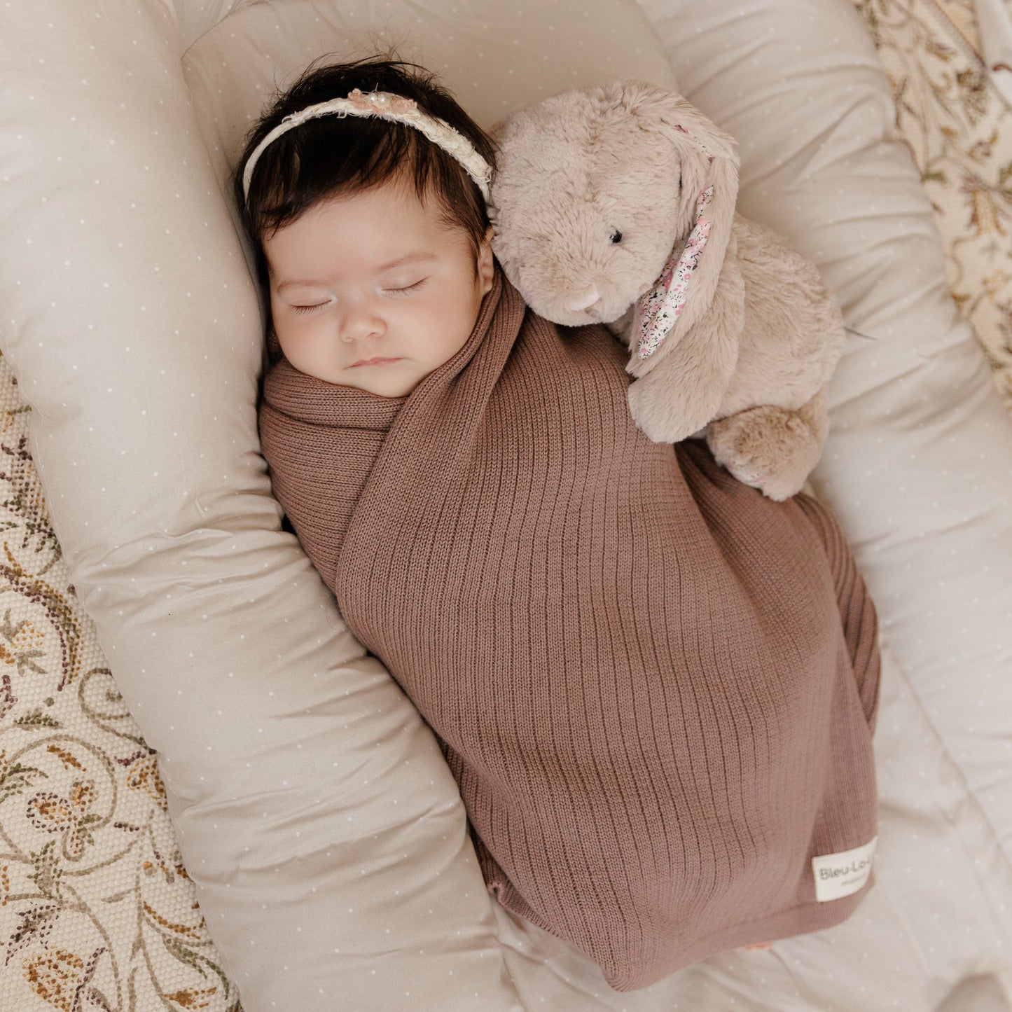 Newborn baby wrapped in a brown swaddle with a plush toy on a soft surface
