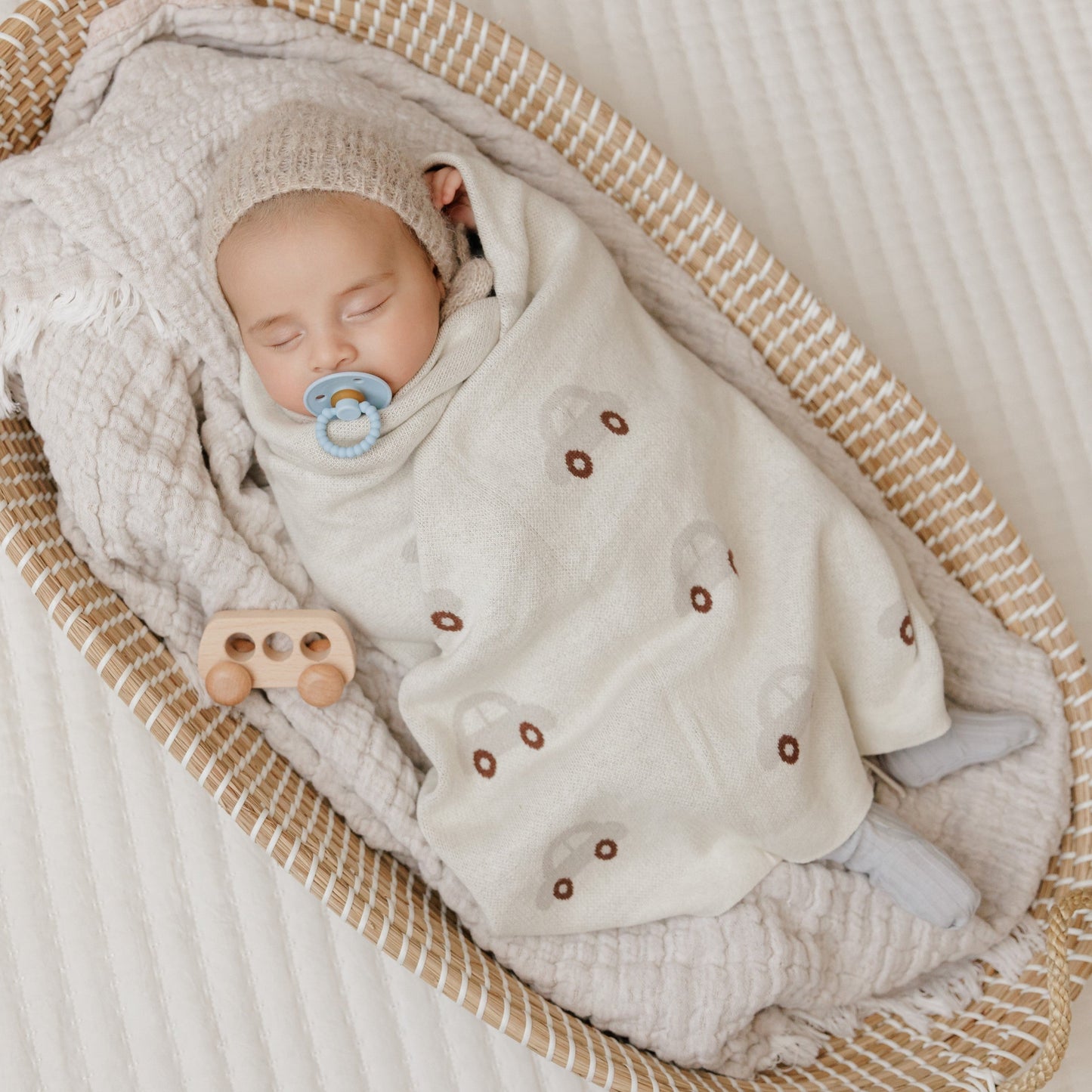 Newborn baby wrapped in a textured blanket with a pacifier, lying in a woven basket.