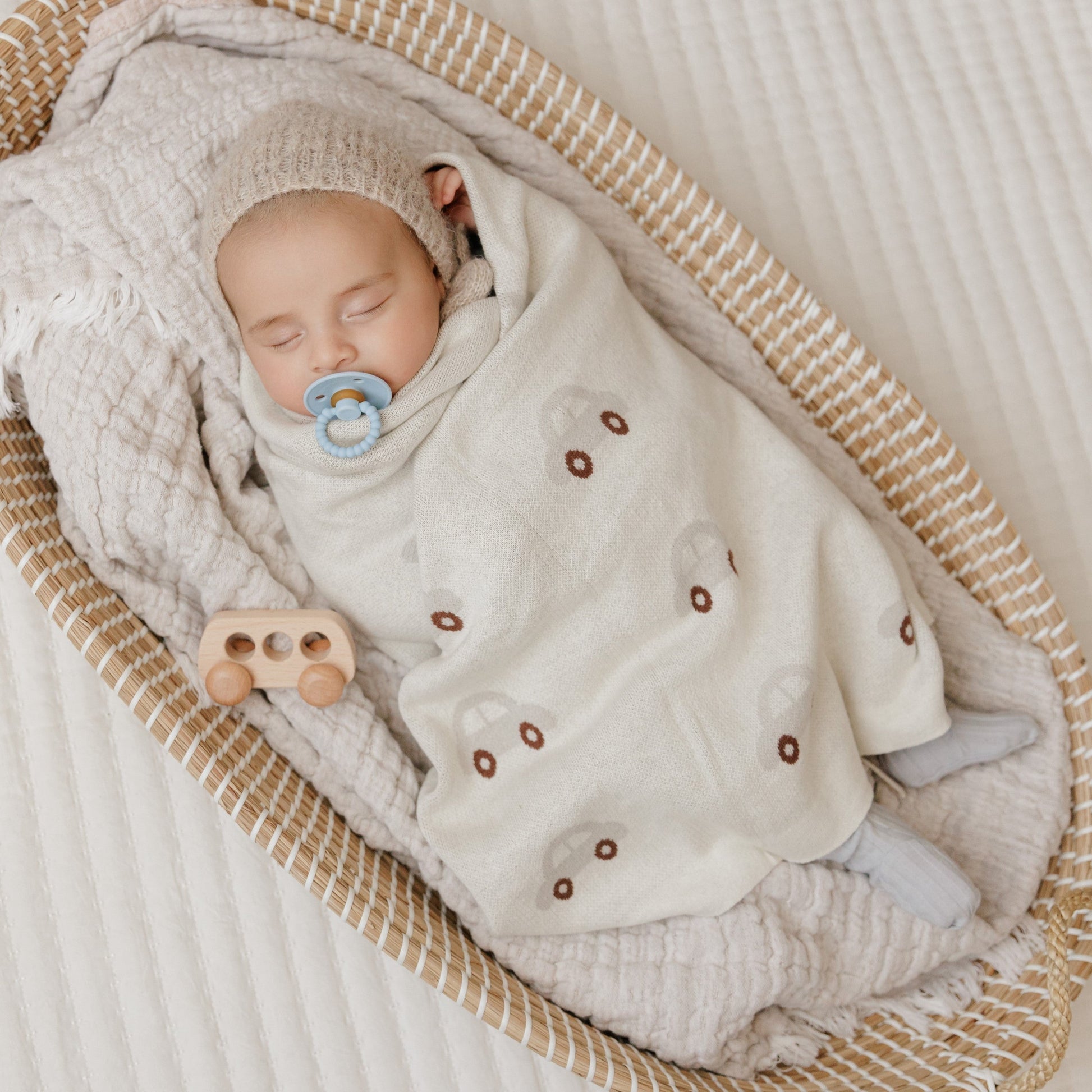 Newborn baby wrapped in a textured blanket with a pacifier, lying in a woven basket.