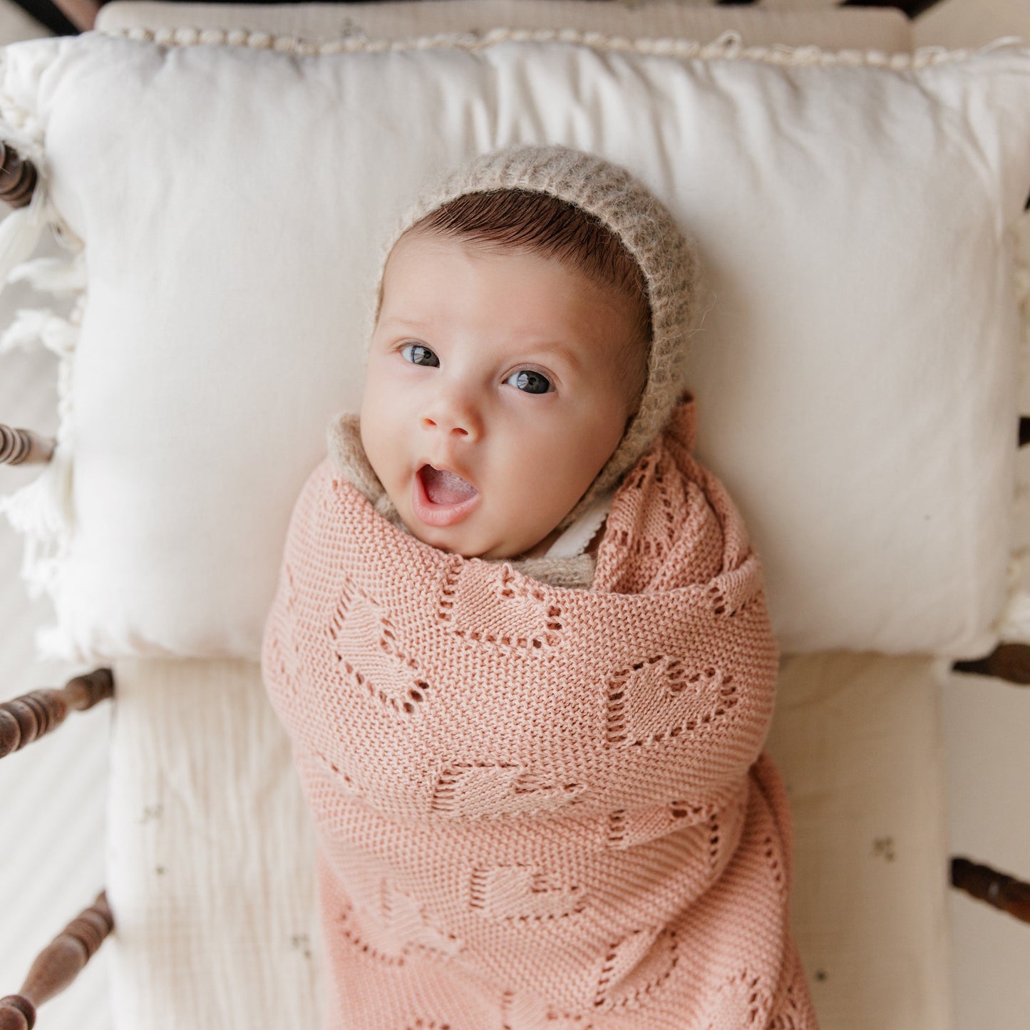 Baby wrapped in a pink Bleu-la-la  blanket with a beige hood, lying on a white cushion.