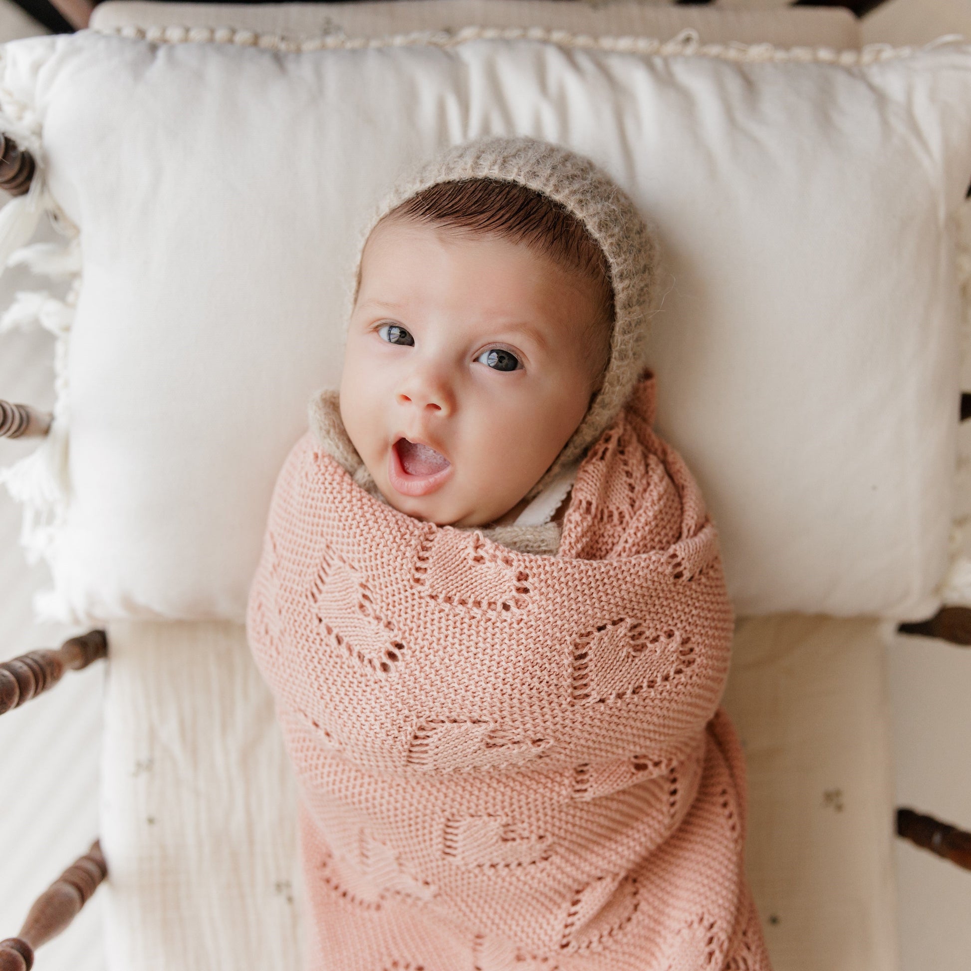 Baby wrapped in a pink Bleu-la-la  blanket with a beige hood, lying on a white cushion.