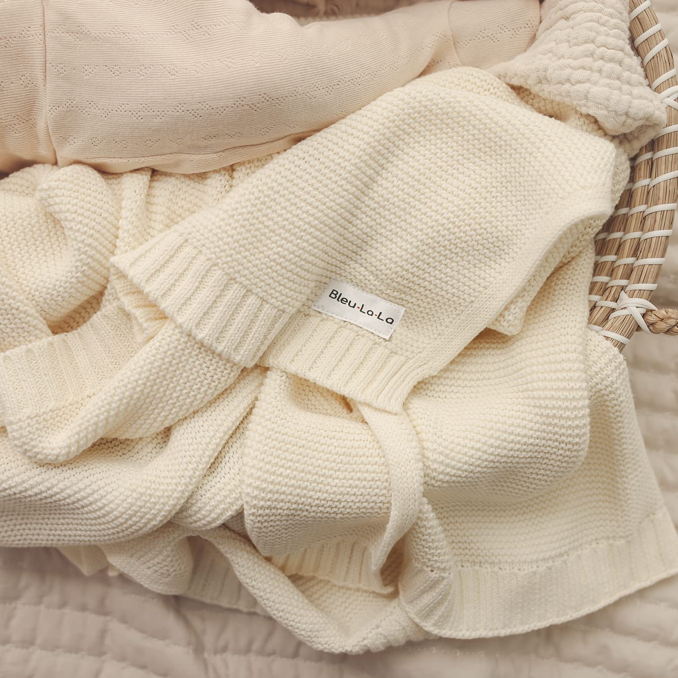 Cream-colored knit Blue-La-La blanket with a brand label on a textured surface