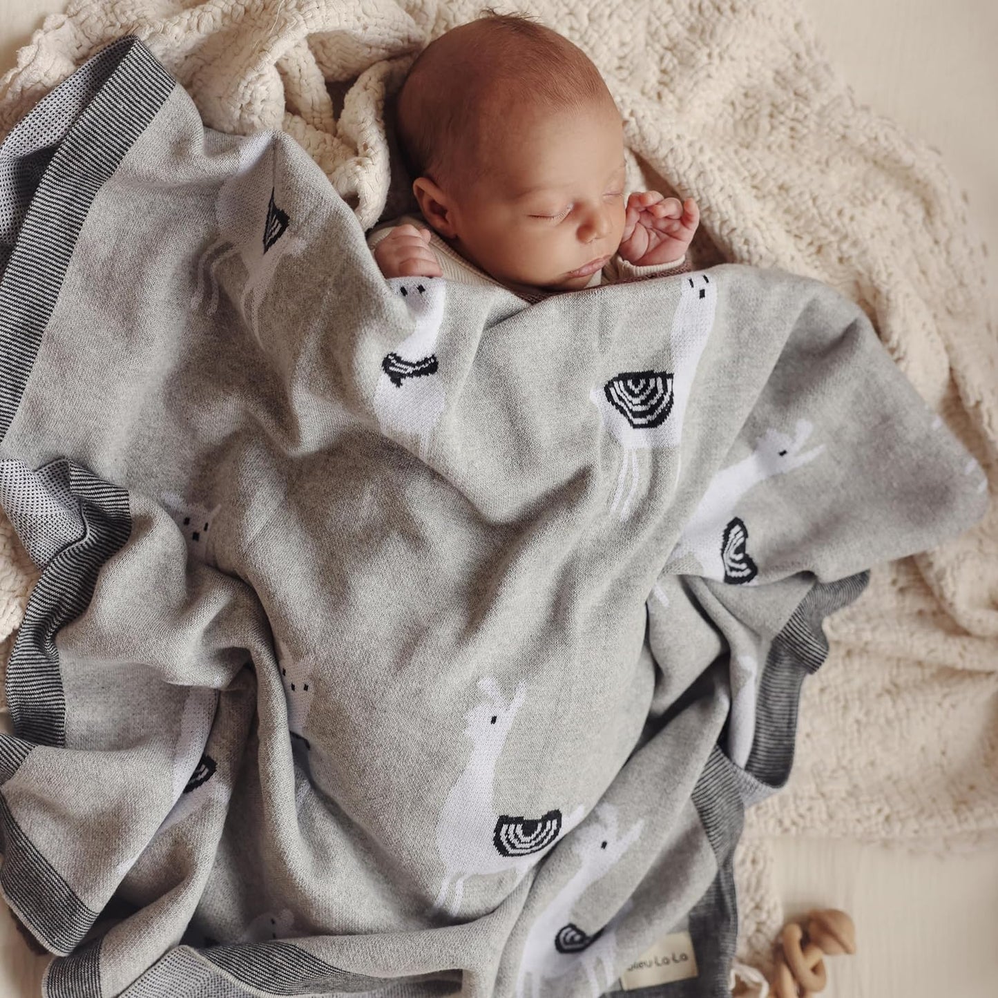 Newborn baby wrapped in a gray blanket with black and white llama patterns on a soft surface