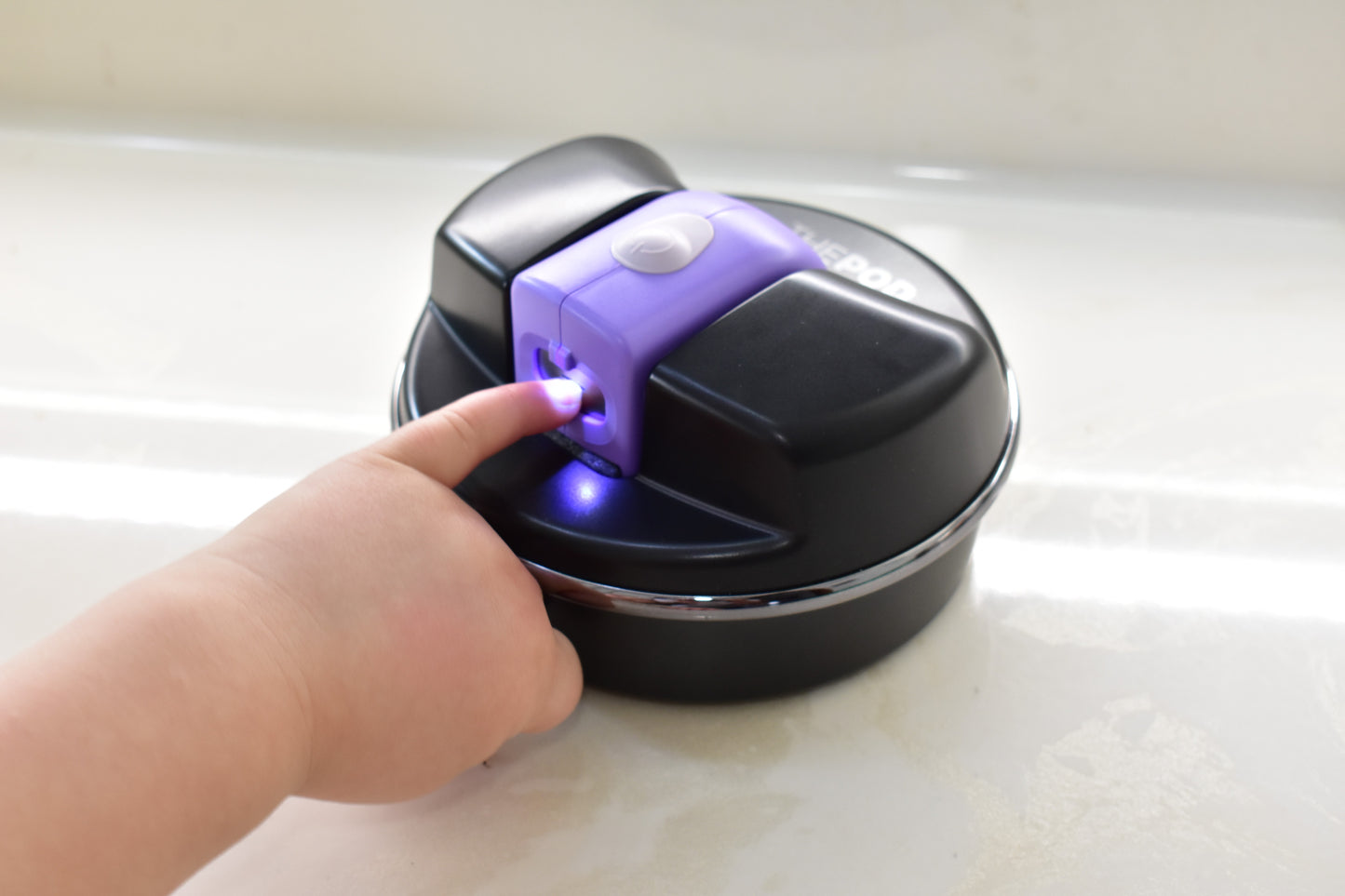 A toddler is using the Pod with a purple infant size Lil Nipper. The bright LED light is shining on the little finger and their nail is inside the safety slot being trimmed.