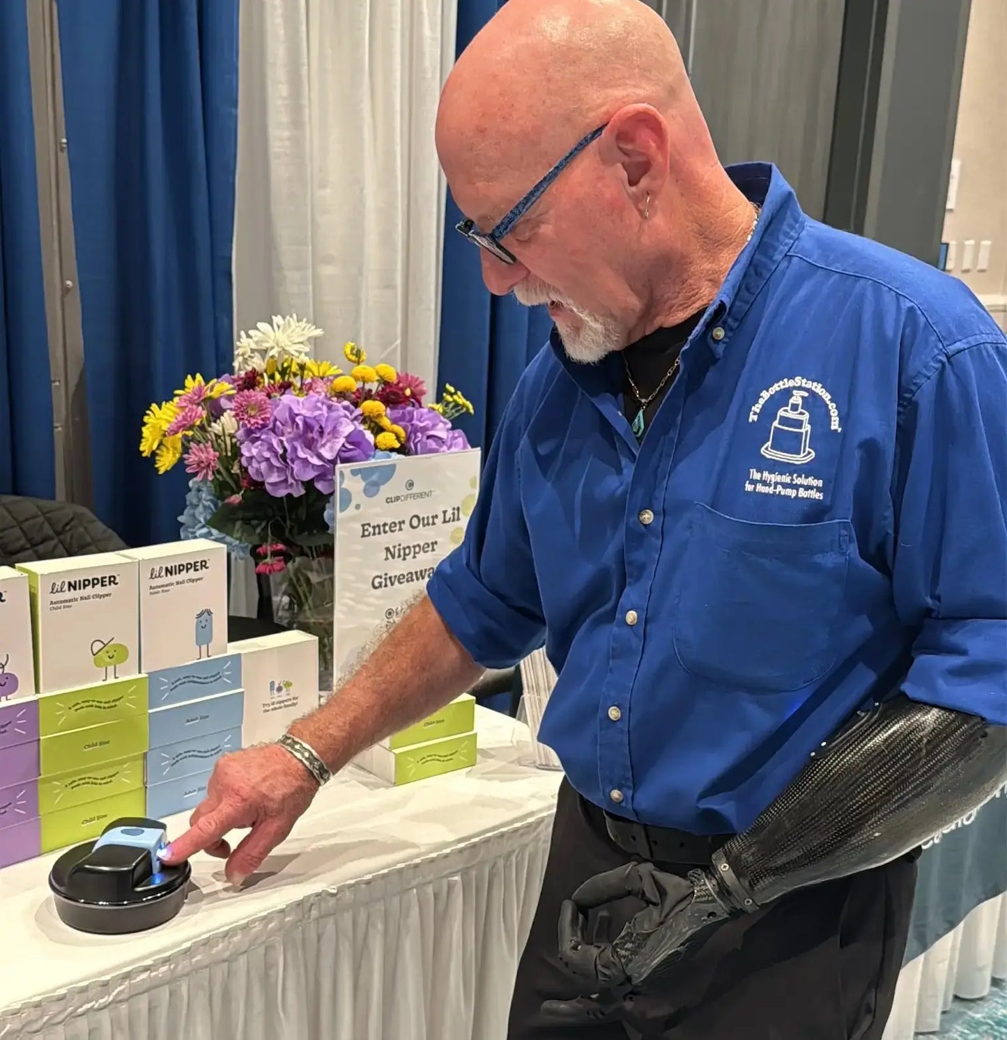Man in a blue shirt and one arm using The POD and Adult Lil Nipper electric nail clipper. He is at a trade show booth.