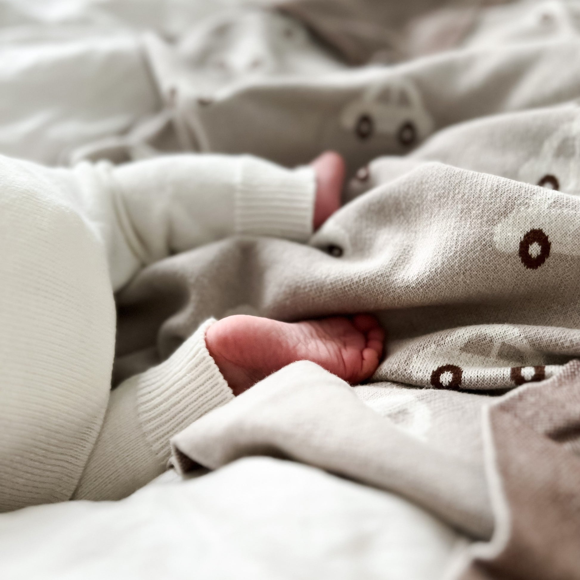 Close-up of a baby's feet in beige socks with paw prints on a soft surface.