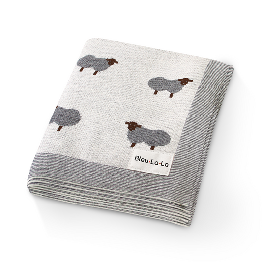 Folded blanket with sheep pattern and 'Bleu Lo La' label on a white background