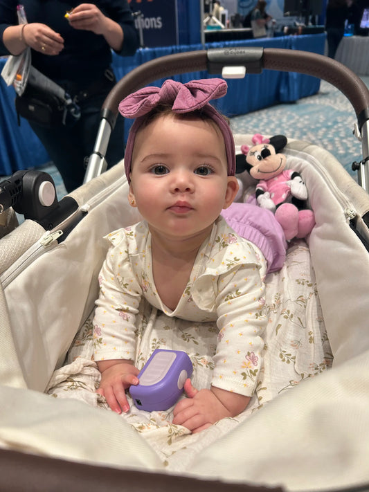 Precious baby girl with a pink bow and big brown eyes in her carrier holding a Lil Nipper nail clipper. 