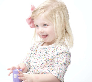A little girl using the infant lil nipper nail clipper in purple color - infant and toddler size. She has her tongue sticking out and smiling.