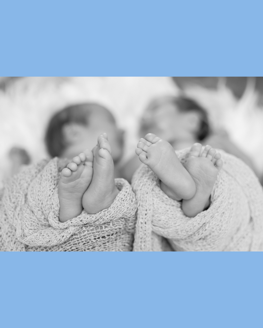 Black and white image of twin babies sleeping, their faces are blurred and the focus is on their feet.