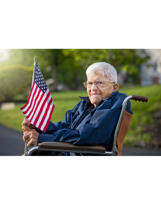 An older veteran in a wheelchair holding an American flag.