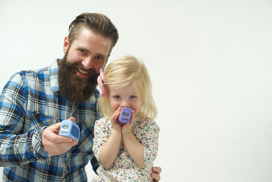 warm, engaging photograph of a dad and toddler (around age 2) sitting together at a child-sized table with a "nail care station" set up with the Lil Nipper infant size in her hand