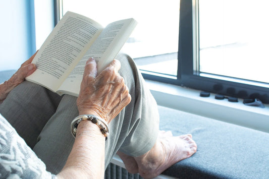 An elderly woman with her feet up relaxing and reading a book.