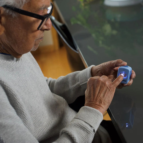 Senior man with glasses using a blue electronic nail clipper device in front of him. The clipper has a bright LED light.