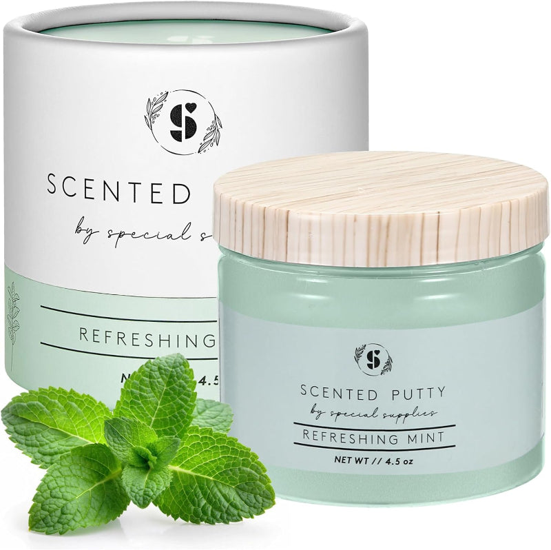 Jar of scented putty with a wooden lid, surrounded by mint leaves on a white background.