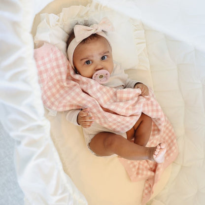Baby wrapped in a pink checkered blanket with a pacifier, wearing a headband.