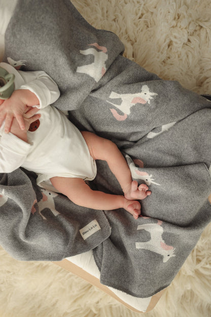 Baby wrapped in a gray blanket with unicorn patterns on a soft surface