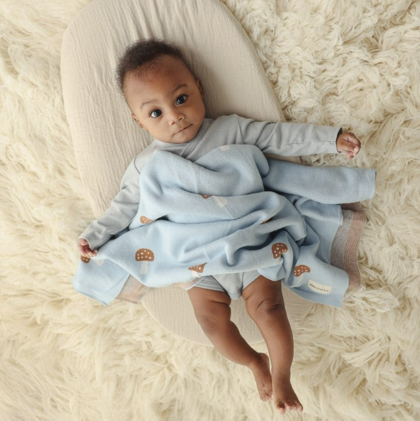 Baby lying on a fluffy white surface with a light blue blanket with a mushroom pattern