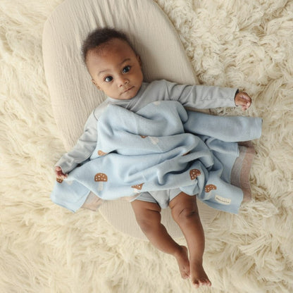Baby lying on a fluffy white surface with a light blue blanket with a mushroom pattern