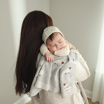Woman holding a baby wrapped in a gray blanket with a neutral background